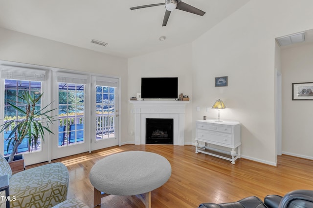 living area featuring a ceiling fan, lofted ceiling, a tiled fireplace, baseboards, and wood finished floors