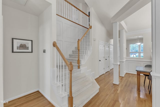 stairs featuring wood finished floors, ornate columns, crown molding, and baseboards