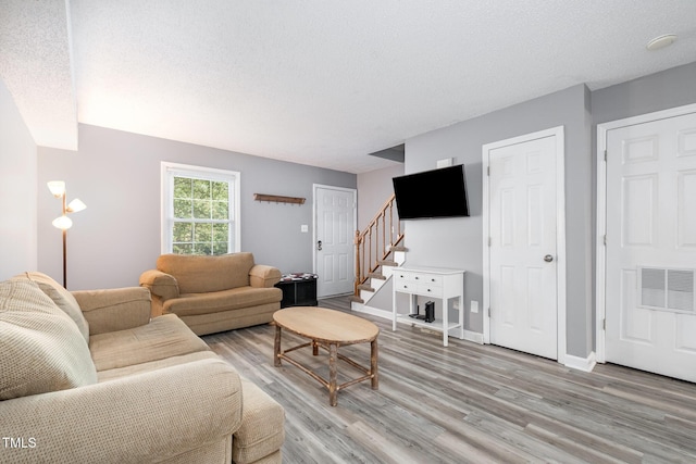 living area featuring light wood-style floors, stairway, a textured ceiling, and visible vents