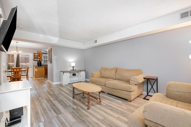 living room with baseboards, an inviting chandelier, visible vents, and light wood-type flooring