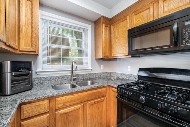 kitchen with light stone counters, a sink, brown cabinets, and black appliances