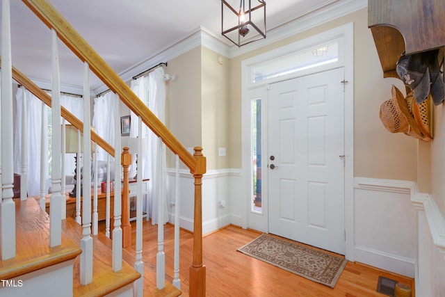 entrance foyer featuring stairs, light wood finished floors, a wainscoted wall, crown molding, and a chandelier