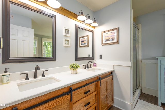 bathroom featuring wainscoting, double vanity, a shower with door, and wood finished floors