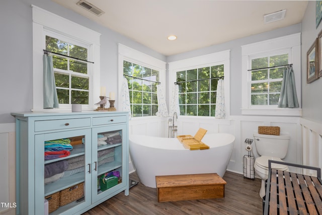 bathroom with a decorative wall, a wainscoted wall, wood finished floors, a freestanding tub, and recessed lighting