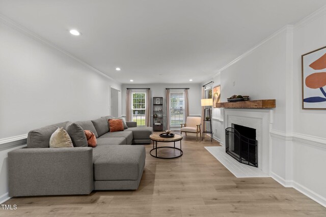 living area featuring a fireplace with flush hearth, recessed lighting, light wood-style floors, ornamental molding, and baseboards