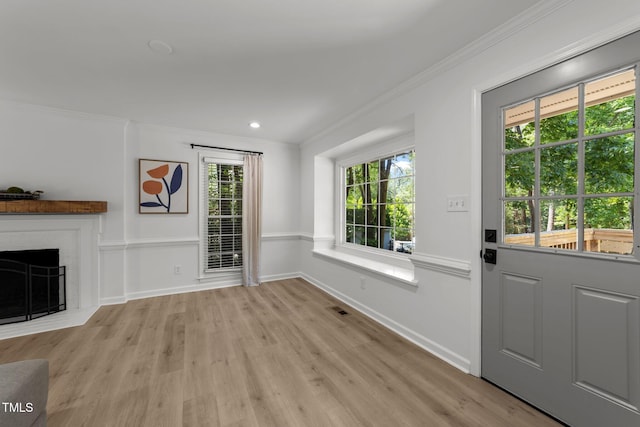 unfurnished living room with light wood-style floors, crown molding, baseboards, and a brick fireplace