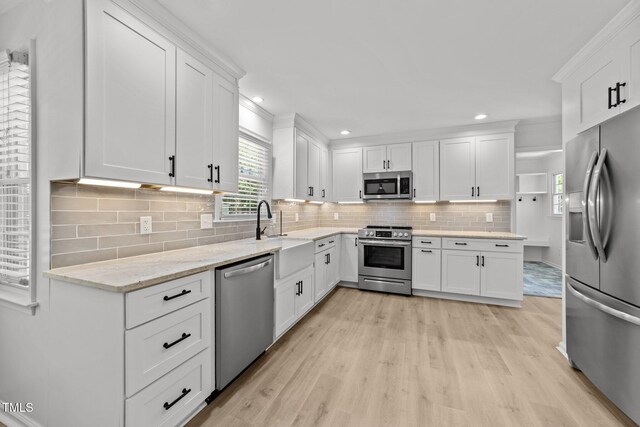 kitchen with appliances with stainless steel finishes, a sink, white cabinetry, light wood-type flooring, and recessed lighting