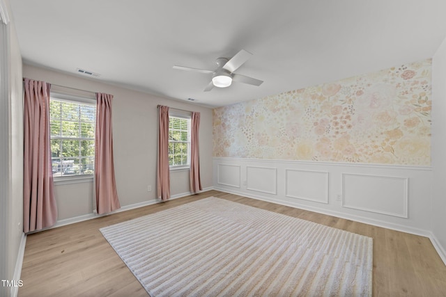 spare room with wallpapered walls, a wainscoted wall, ceiling fan, light wood-style flooring, and baseboards