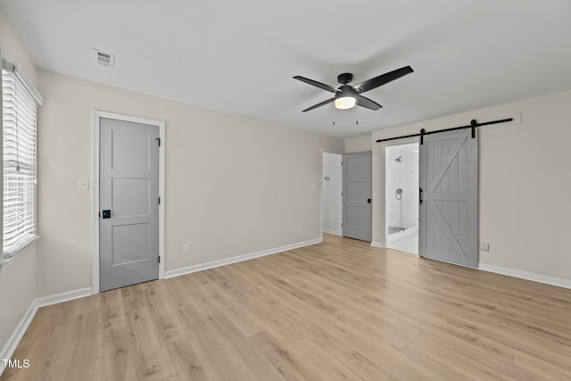 unfurnished bedroom with a barn door, light wood-type flooring, and baseboards