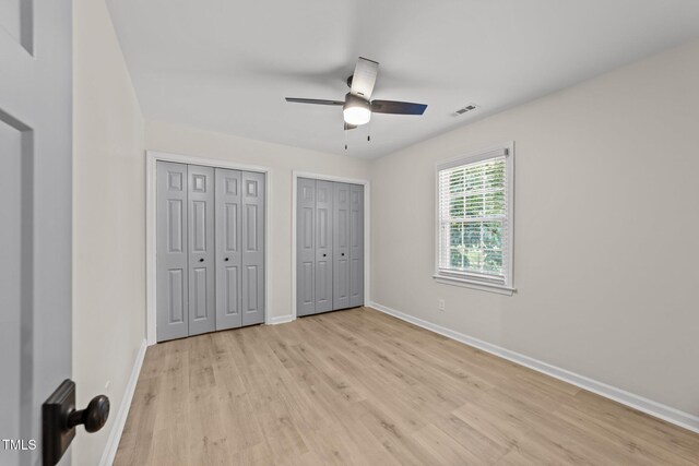 unfurnished bedroom with light wood finished floors, two closets, baseboards, and ceiling fan