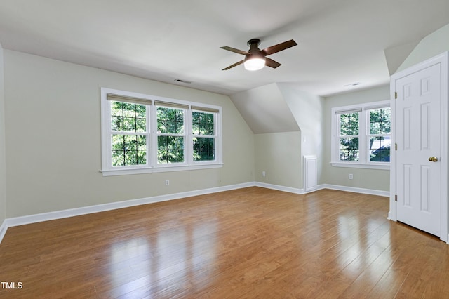 additional living space with ceiling fan, healthy amount of natural light, wood finished floors, baseboards, and vaulted ceiling