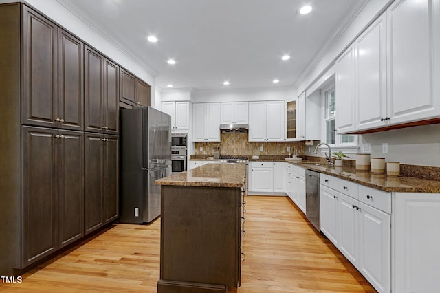 kitchen featuring appliances with stainless steel finishes, under cabinet range hood, light wood finished floors, a kitchen island, and dark stone countertops