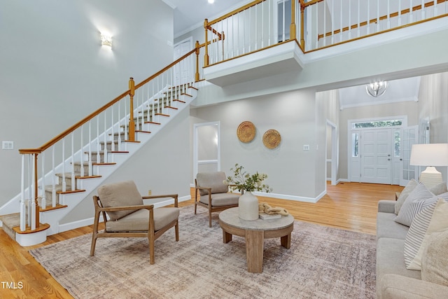 living room featuring stairs, wood finished floors, baseboards, a towering ceiling, and ornamental molding
