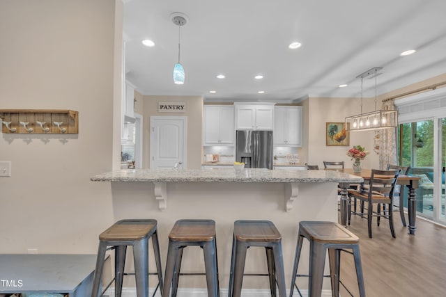 1920 Bright Kannon Way, Wendell, NC 27591 - kitchen featuring stainless steel fridge, white cabinets, a breakfast bar area, light stone counters, and recessed lighting