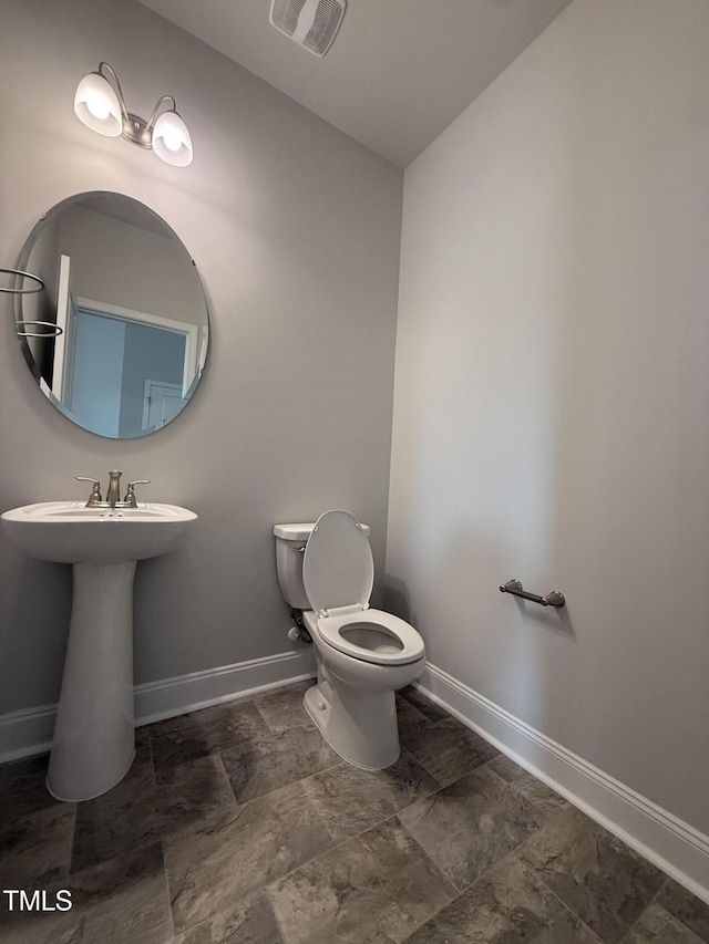 half bath featuring visible vents, a sink, baseboards, and toilet