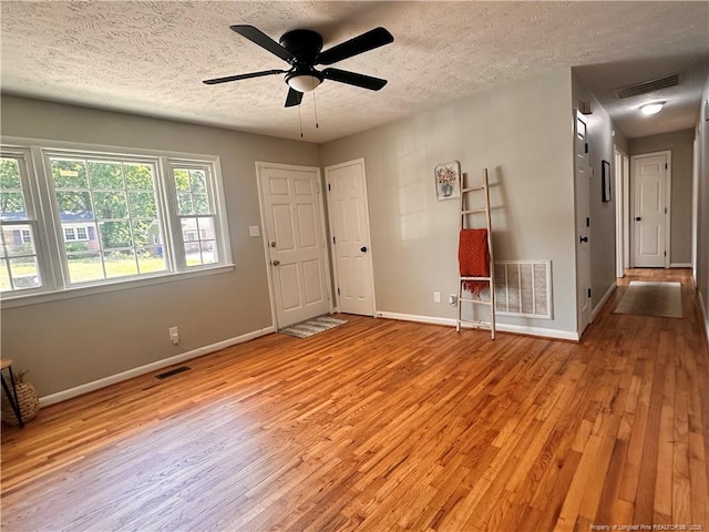 empty room with a textured ceiling, baseboards, light wood-style flooring, and visible vents