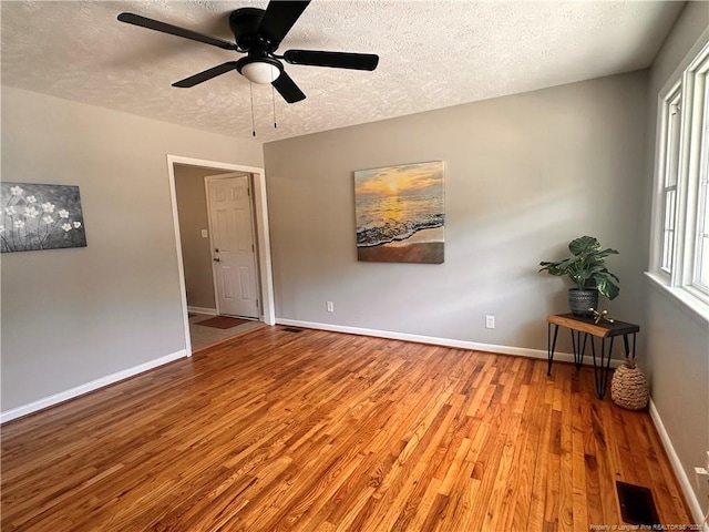 unfurnished room with a textured ceiling, a ceiling fan, baseboards, wood finished floors, and visible vents