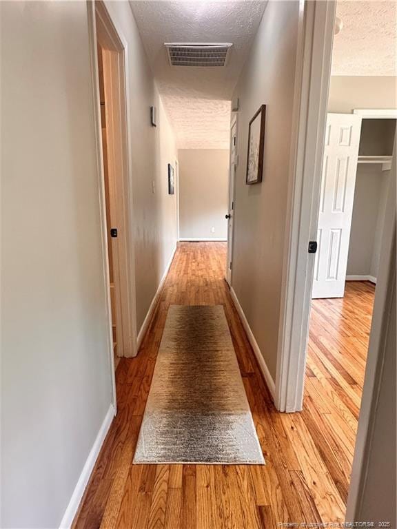hallway with visible vents, baseboards, a textured ceiling, and wood finished floors