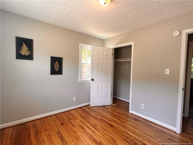 unfurnished bedroom with baseboards, a textured ceiling, wood finished floors, and a closet
