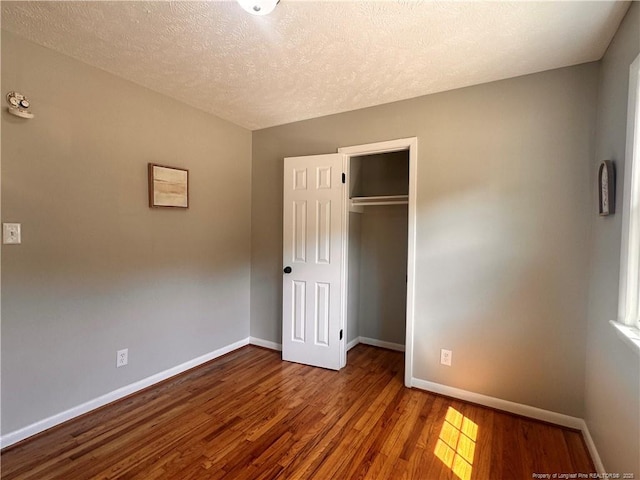 unfurnished bedroom featuring baseboards, a textured ceiling, wood finished floors, and a closet