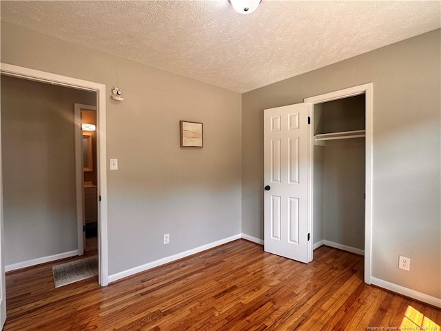 unfurnished bedroom featuring a textured ceiling, baseboards, a closet, and wood finished floors