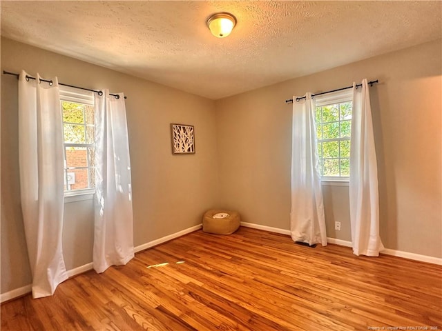 spare room with a textured ceiling, baseboards, and light wood-type flooring