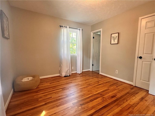 unfurnished bedroom featuring baseboards, a textured ceiling, and wood finished floors