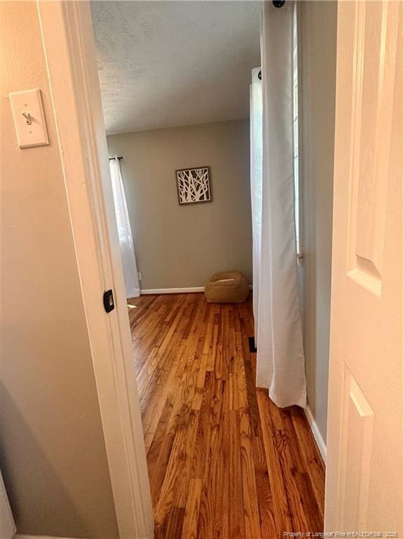 hallway with baseboards, a textured ceiling, and light wood-style flooring