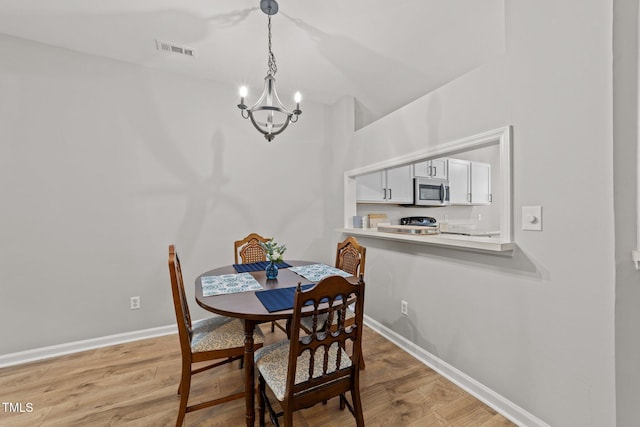 dining area featuring a chandelier, light wood finished floors, baseboards, and vaulted ceiling