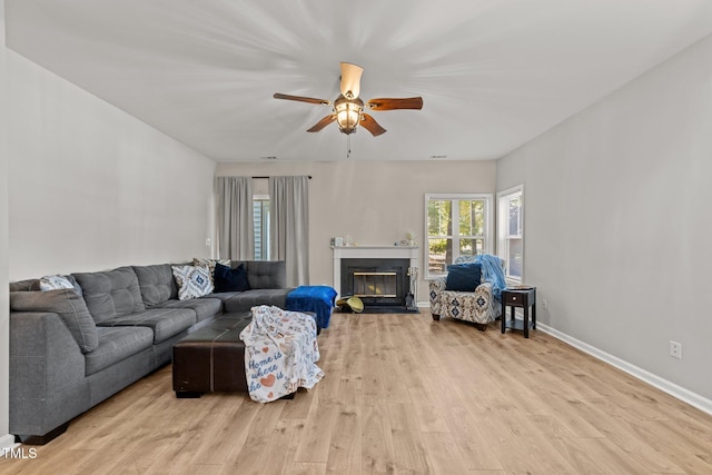 living room featuring ceiling fan, wood finished floors, baseboards, and a fireplace with flush hearth