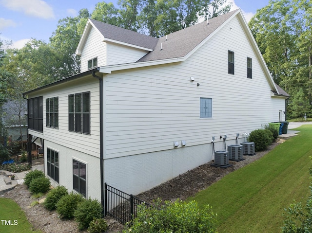 view of side of property featuring a lawn, central air condition unit, and a shingled roof