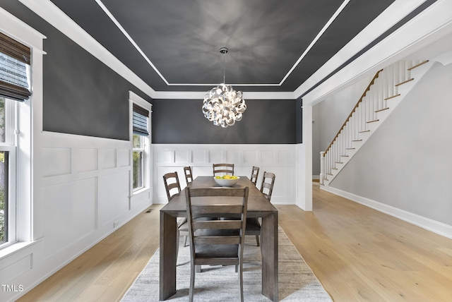 dining room featuring a tray ceiling, wood finished floors, stairway, an inviting chandelier, and a decorative wall