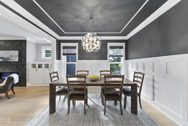 dining area with light wood-type flooring, a chandelier, a decorative wall, and a tray ceiling