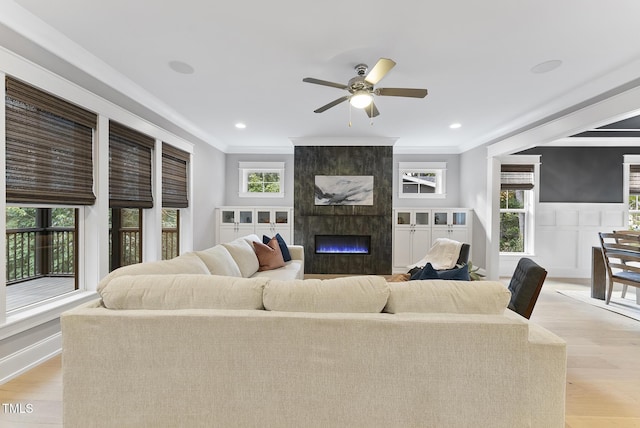 living room featuring crown molding, a fireplace, a ceiling fan, and light wood-style flooring