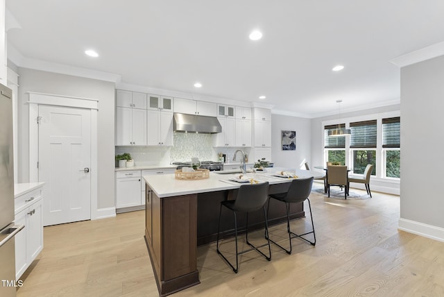 kitchen with crown molding, light countertops, light wood-style flooring, tasteful backsplash, and under cabinet range hood