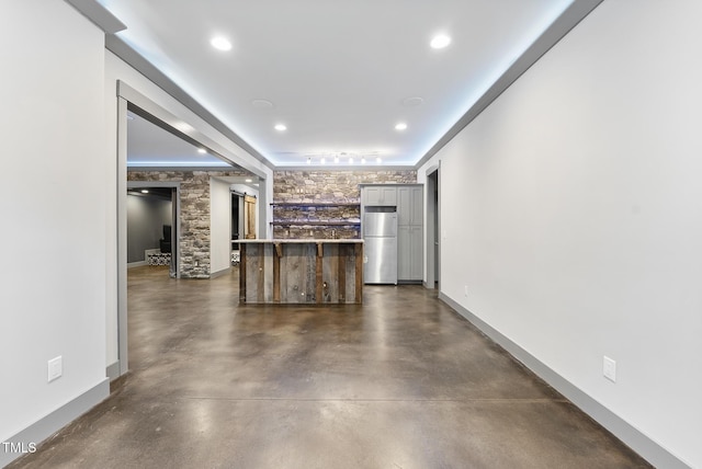 kitchen featuring baseboards, freestanding refrigerator, concrete flooring, and a kitchen breakfast bar