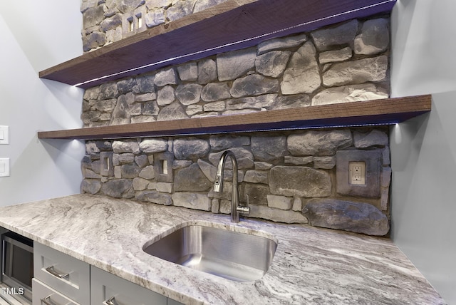 room details with stainless steel microwave, light stone countertops, a sink, and open shelves