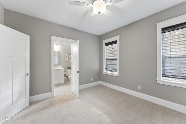 unfurnished bedroom featuring light colored carpet, a ceiling fan, baseboards, and ensuite bath
