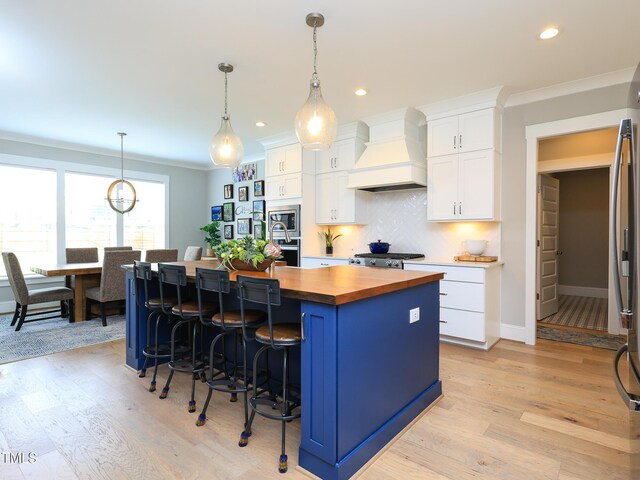 1180 Duke Farm Dr, Wake Forest, NC 27587 - kitchen with butcher block countertops, custom range hood, an island with sink, white cabinetry, and light wood-style floors