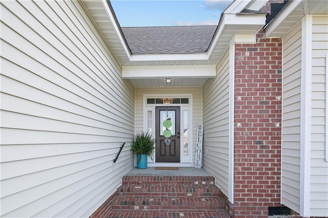 entrance to property featuring brick siding and roof with shingles