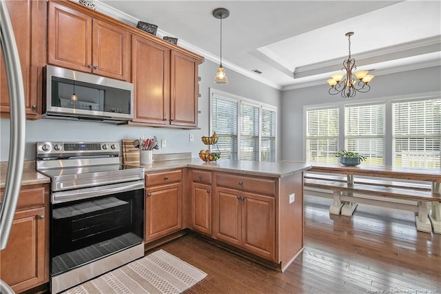 kitchen featuring appliances with stainless steel finishes, brown cabinets, dark wood finished floors, light countertops, and a peninsula