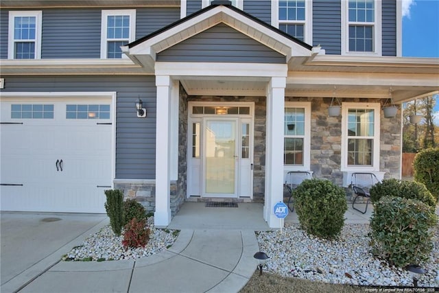 view of exterior entry featuring a porch, an attached garage, stone siding, and concrete driveway