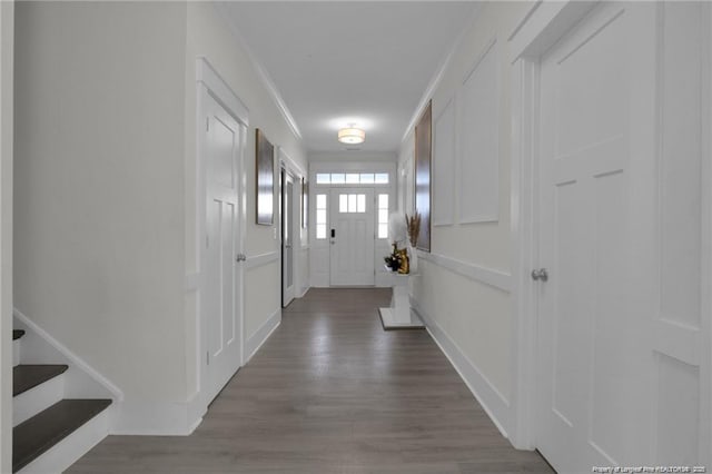 corridor with ornamental molding, a decorative wall, dark wood-style flooring, and stairs