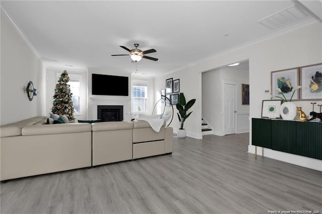 living area featuring a ceiling fan, visible vents, ornamental molding, and a glass covered fireplace