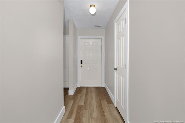 hall featuring baseboards, a textured ceiling, and light wood finished floors