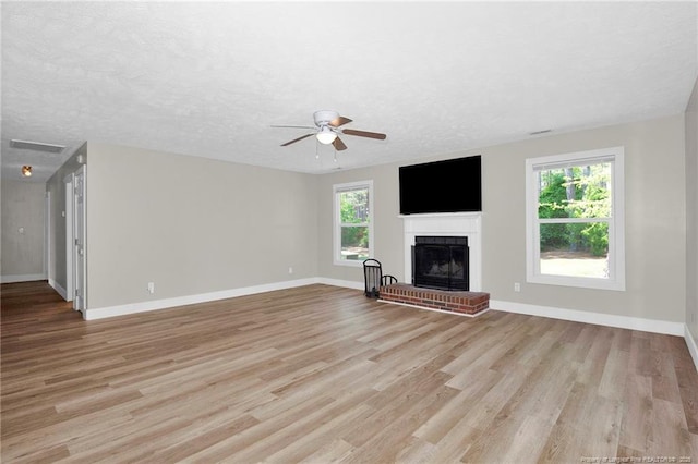 unfurnished living room with light wood-type flooring, a brick fireplace, ceiling fan, and baseboards