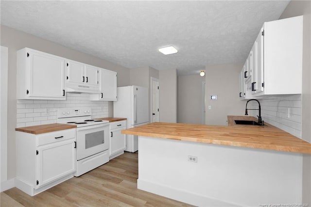 kitchen featuring a sink, a peninsula, butcher block counters, under cabinet range hood, and white appliances