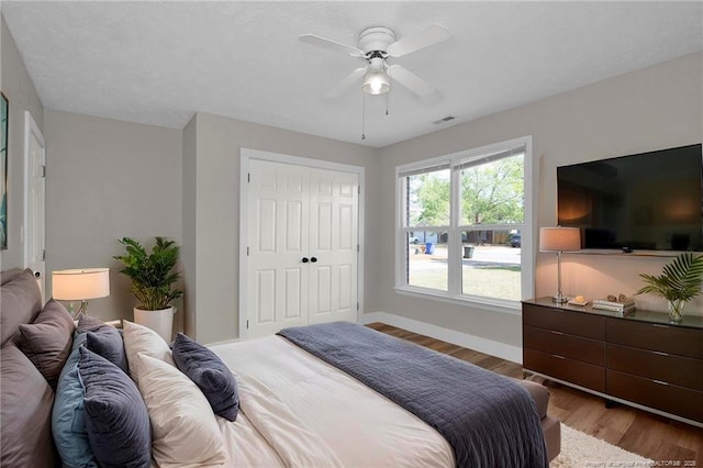 bedroom featuring visible vents, a closet, wood finished floors, baseboards, and a ceiling fan