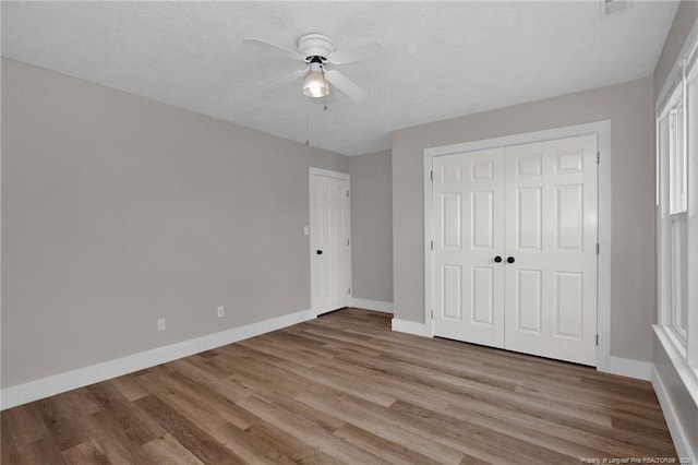 unfurnished bedroom with a closet, wood finished floors, baseboards, a textured ceiling, and a ceiling fan