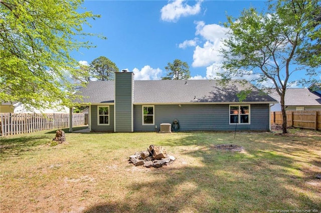 rear view of property with a fenced backyard, a chimney, central air condition unit, a lawn, and a fire pit